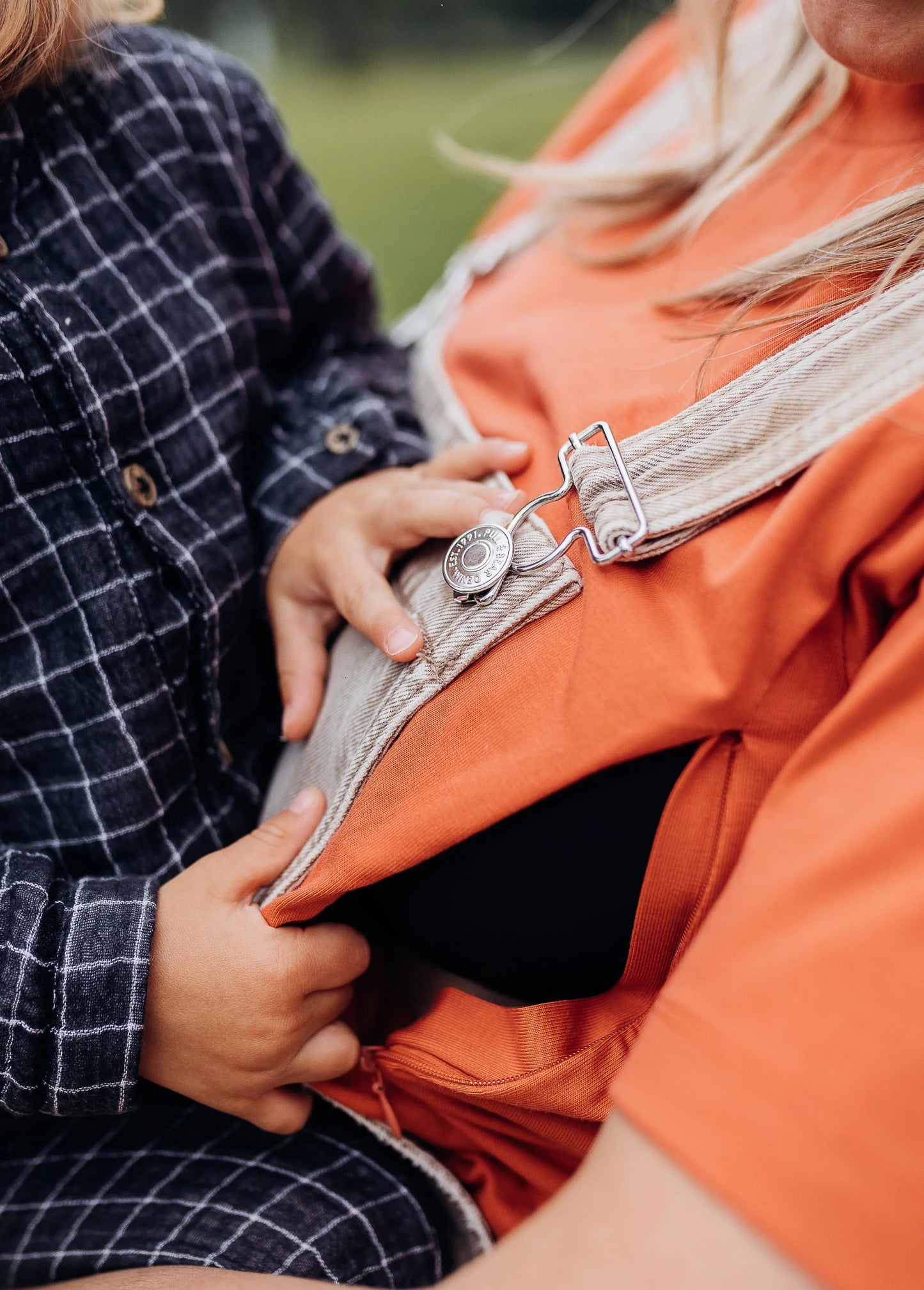 Enfant ouvrant tee-shirt d’allaitement orange à fermeture, gros plan mains et tissu, vêtement pratique.