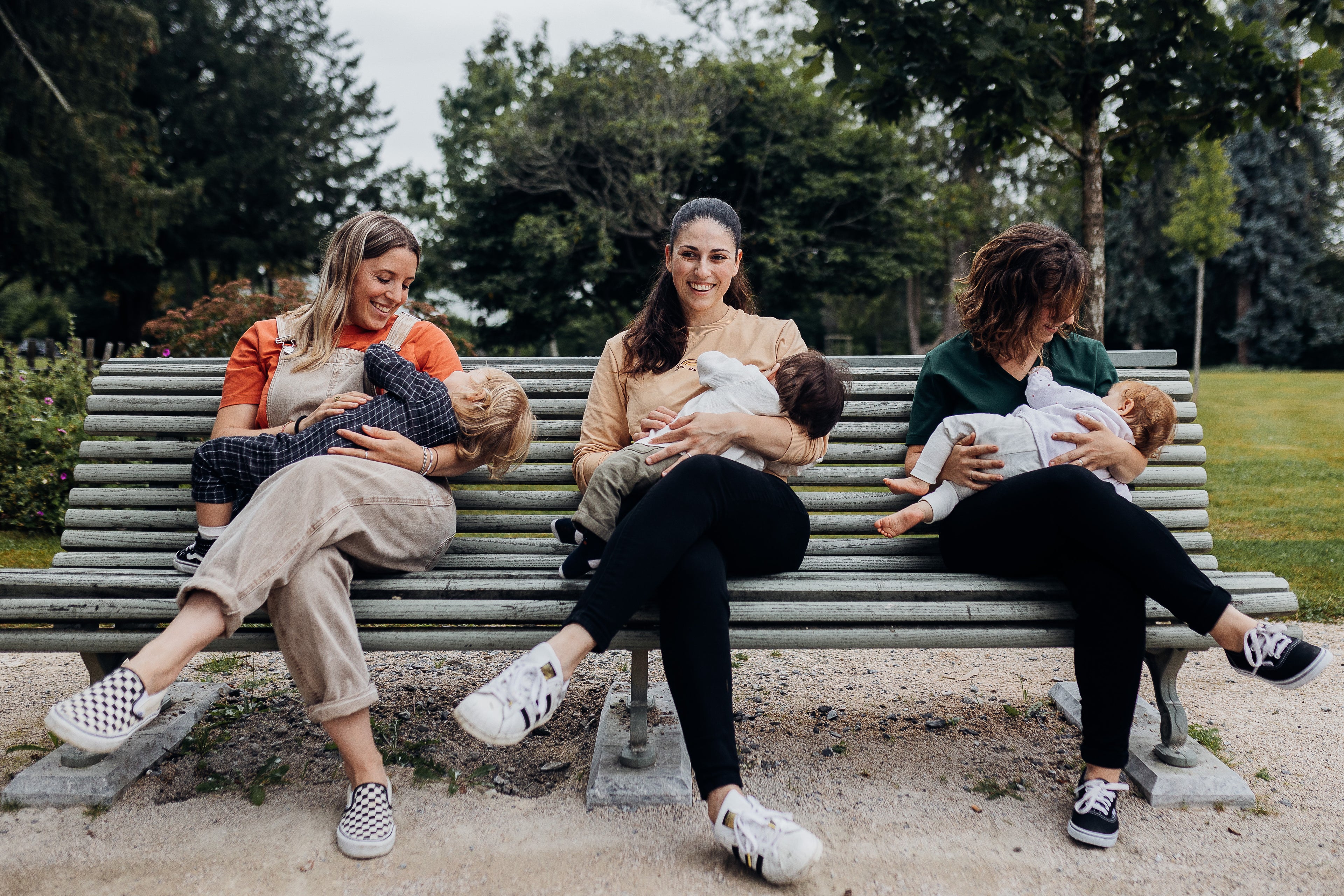 Trois femmes allaitent leur bébé sur un banc dans un parc, vêtements d’allaitement.